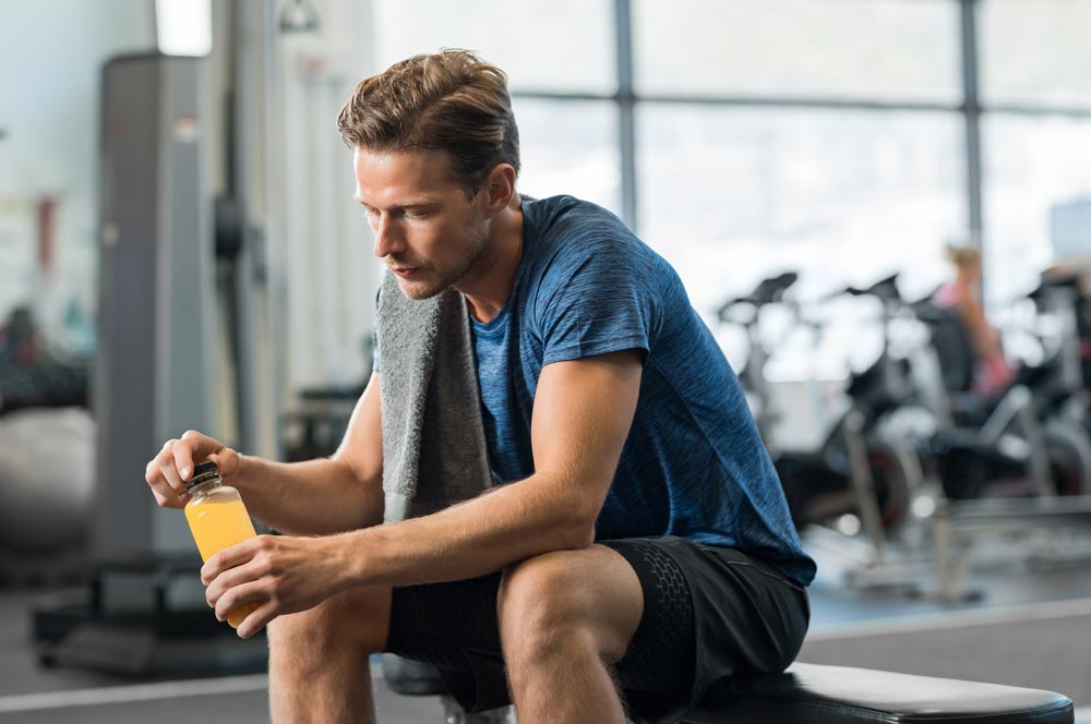 photo of Young man in gym sitting alone opening a bottle of energy drink