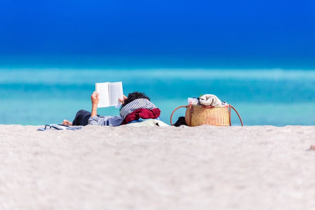 a woman lying on shore reading a book