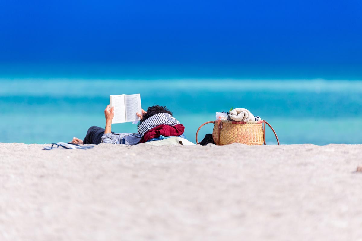 a woman lying on shore reading a book 