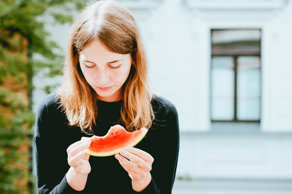 photo of a woman eating a watermelon sitting on a bench