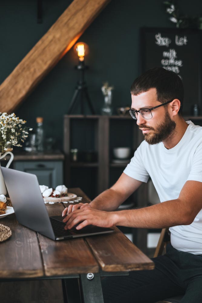 a young caucasian man with beard in front of a laptop working at home