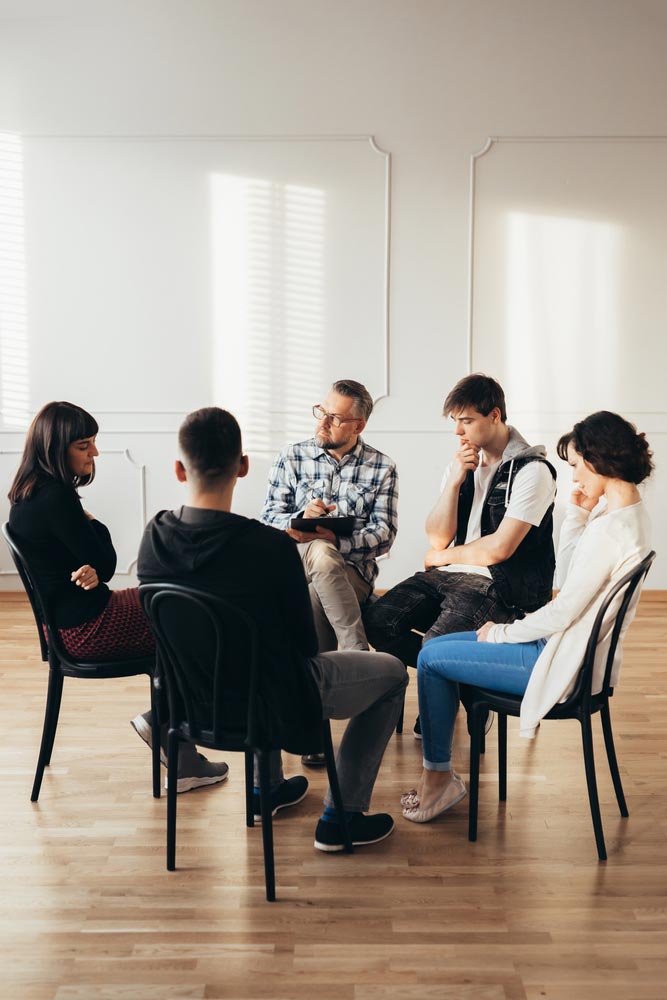 group of people of different ages sits in a circle during group therapy