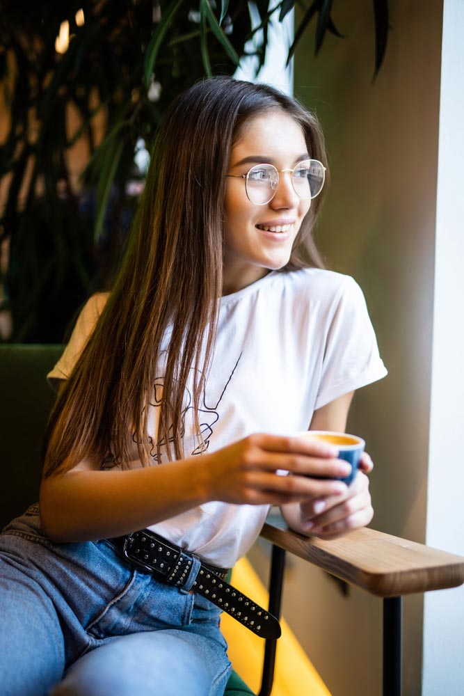 photo of a young lady in white tshirt and jeans smiling and looking outside the window