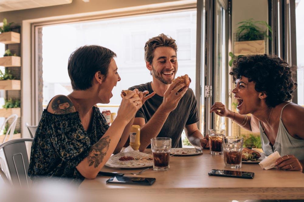three friends laughing and enjoying eating burgers