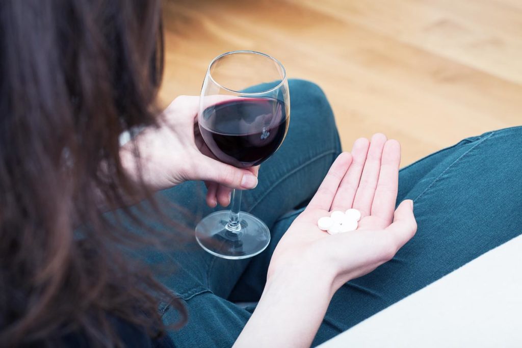 woman holding a glass of wine and xanax tablets