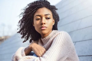 A woman with curly hair sits contemplatively on a wall, reflecting on life's challenges and seeking meaning.