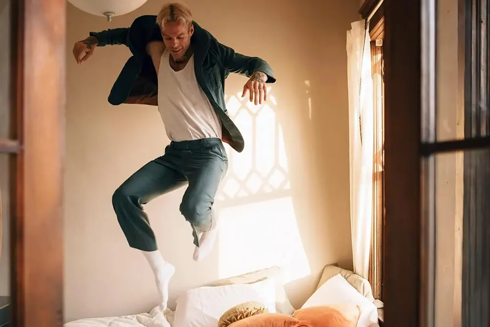 A man with ADHD leaps into the air on a bed embodying a moment of playful spontaneity and vibrant energy