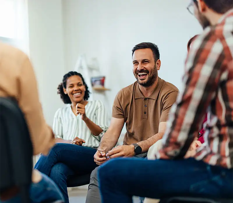 An adult man, looking happy, talking with random people from the group therapy.