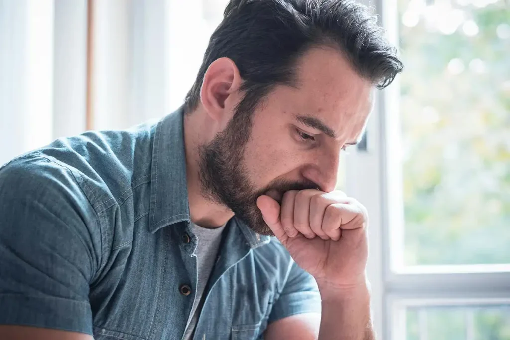 A man sits at a table, resting his chin on his hand, contemplating ways to support someone with depression and alcoholism