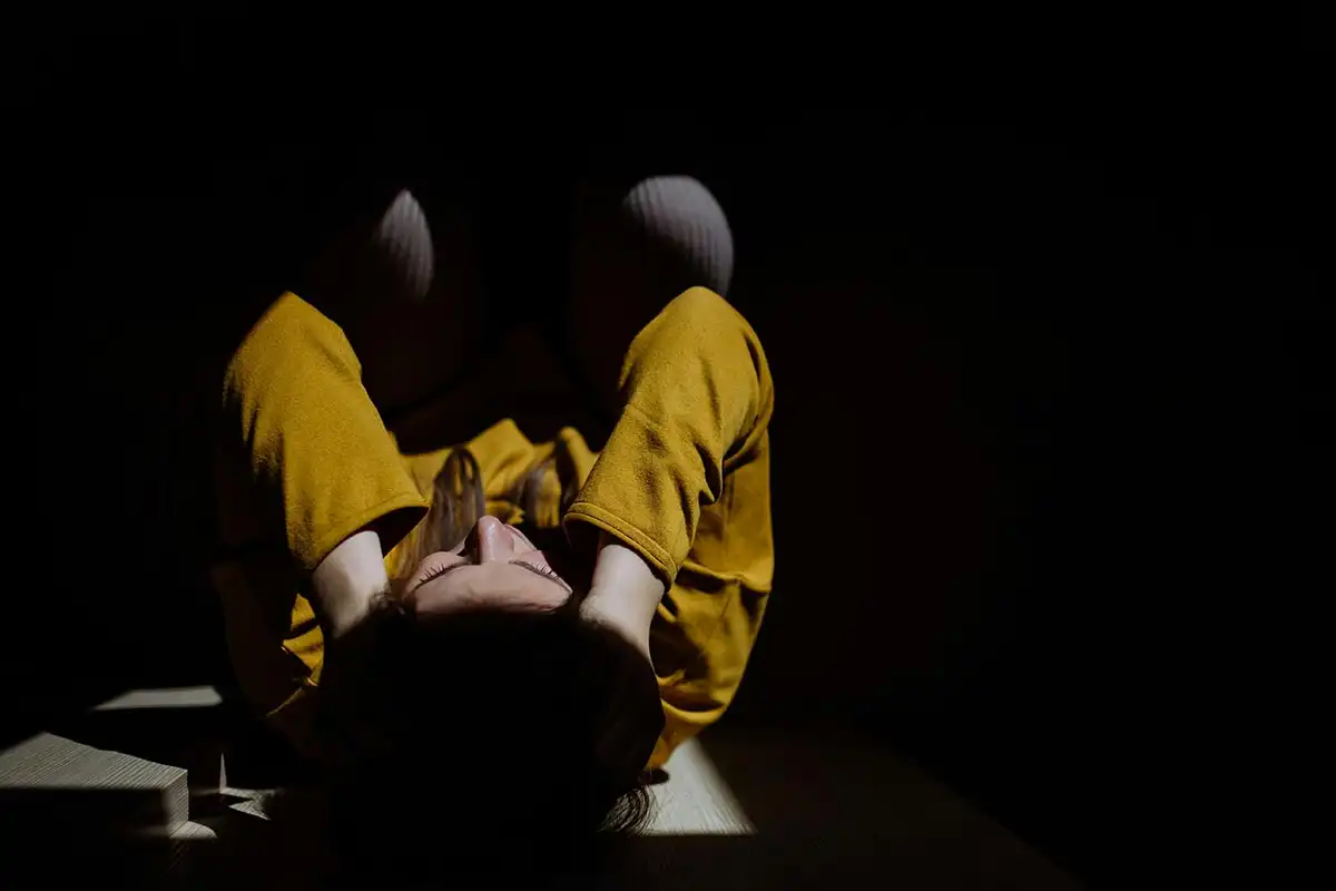 A woman in a yellow outfit sits on the floor, reflecting on trauma triggers and their management.