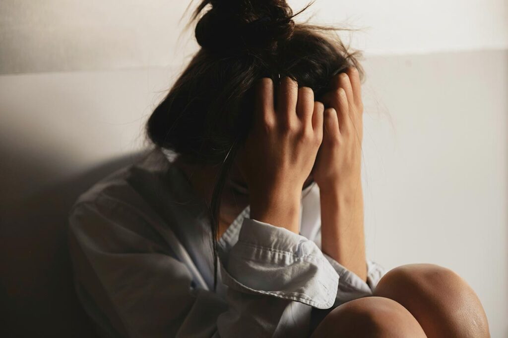 A woman sitting on the floor, hands on her head, reflecting on trauma triggers and their management.