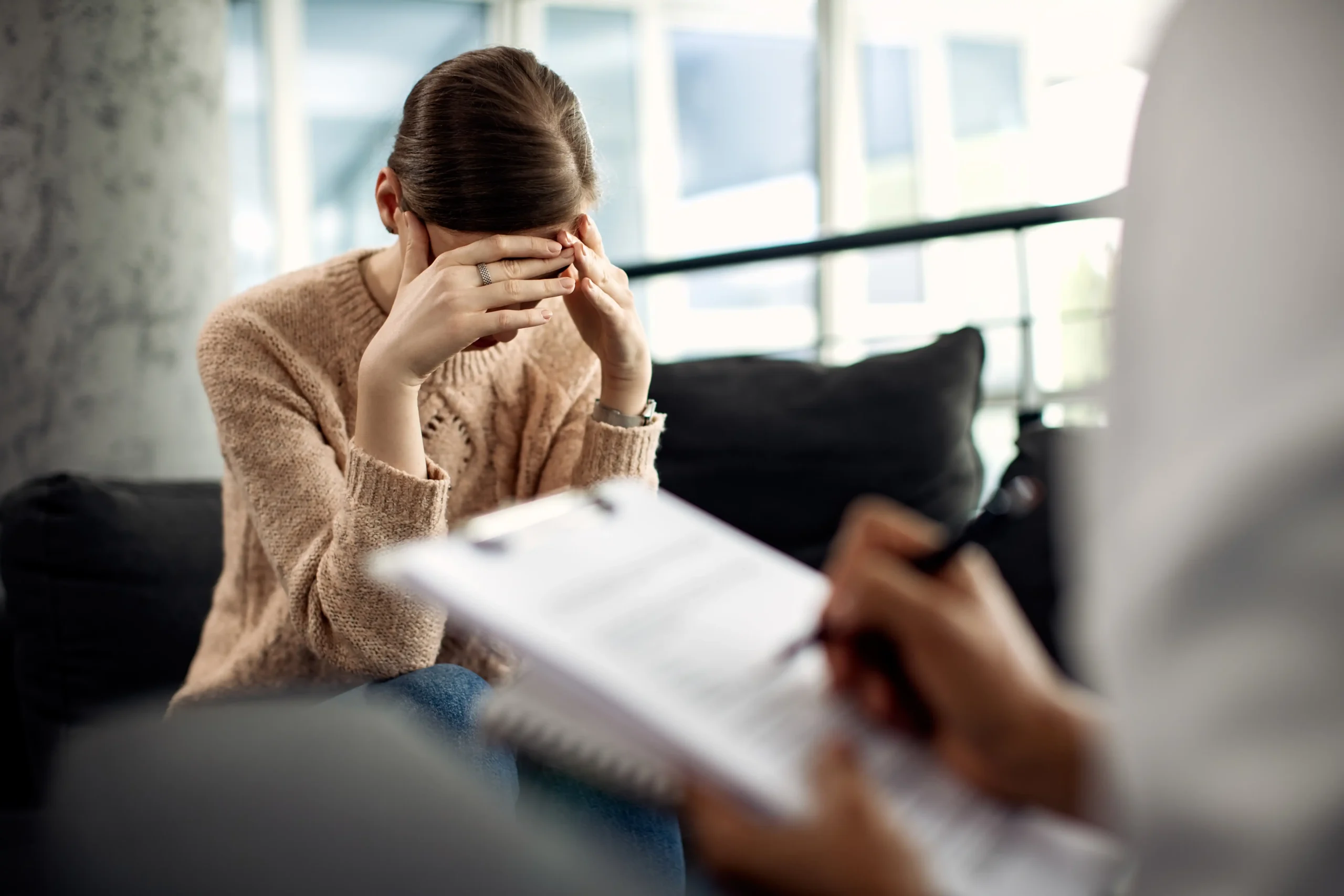 A distressed woman receiving professional mental health support in Laguna Hills, with a therapist taking notes during a counseling session for anxiety and emotional pain.